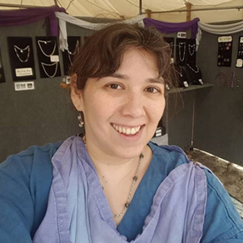 Selfie of the Author. A dark-haired woman wearing black and purple Roman garb smiles at the camera.